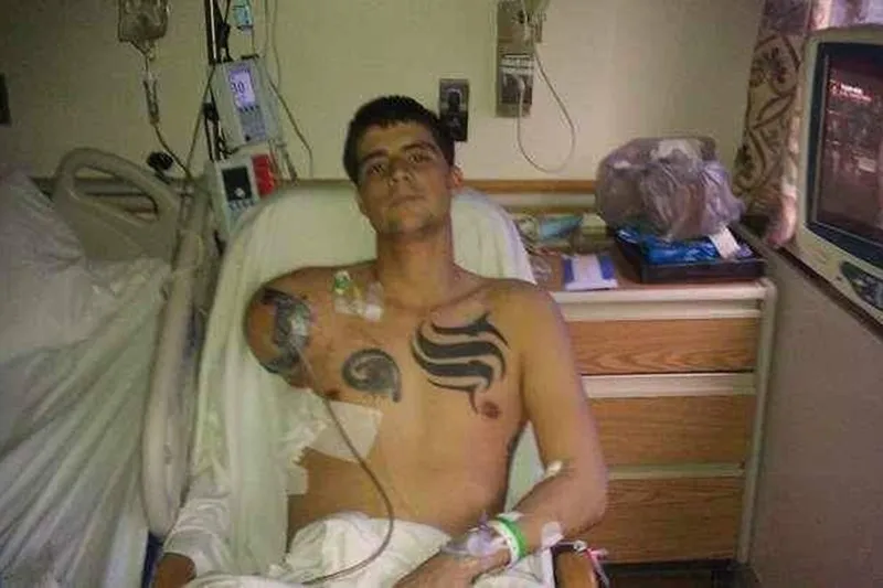 A man sitting in a hospital bed with tattoos on his arms.