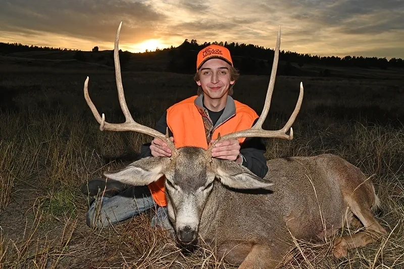 A young man in an orange vest with two large deer.