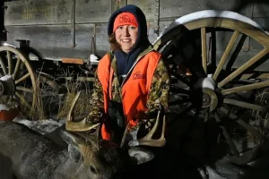 A young person in an orange jacket holding two deer antlers.