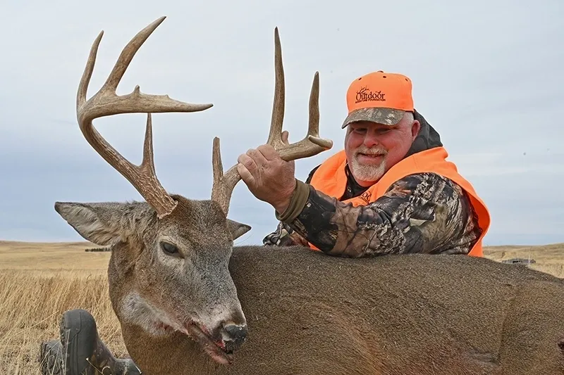 A man in an orange vest is holding on to the horns of his deer.