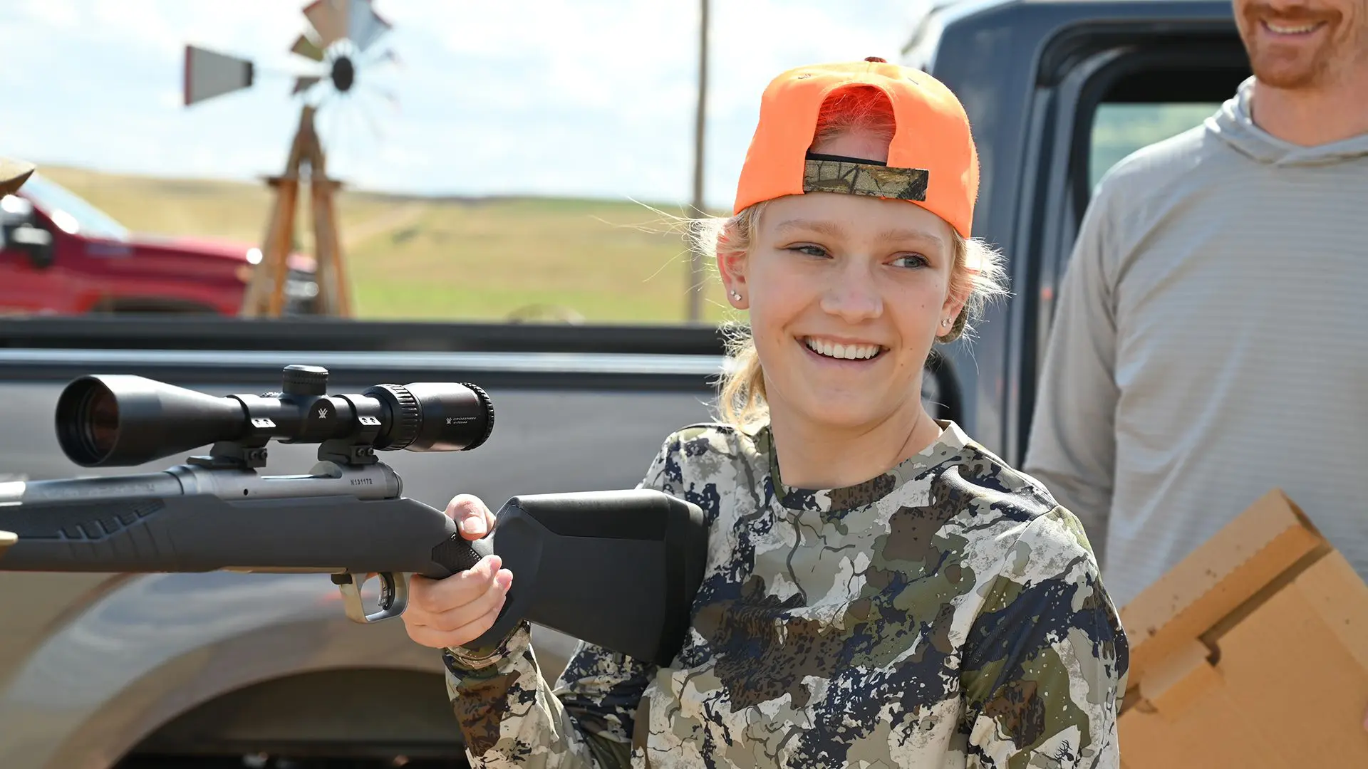 A woman in camouflage holding a rifle and smiling.