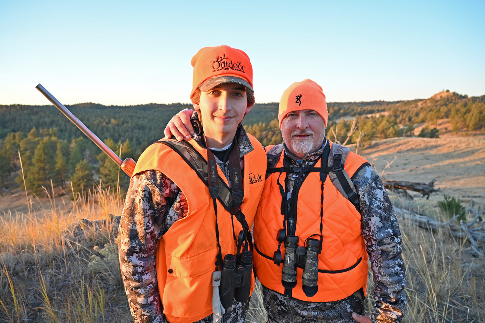 Two men in orange vests and hats standing next to each other.
