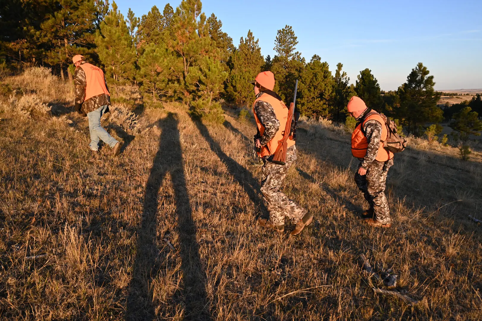 A group of hunters in camouflage gear walking through the grass.