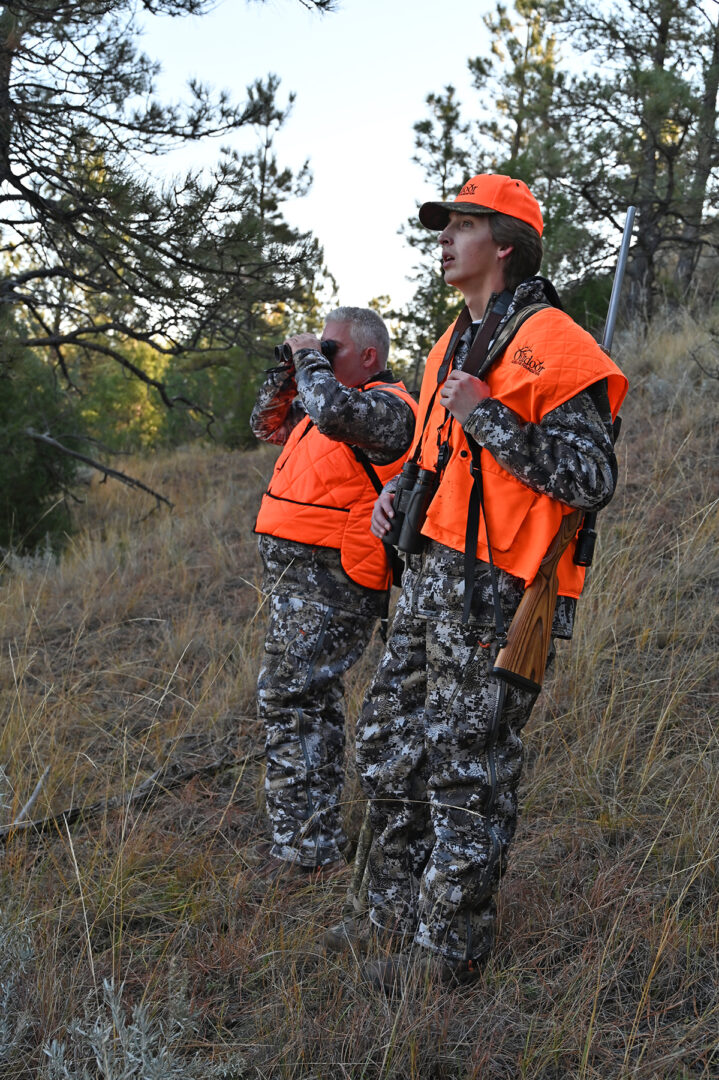 Two hunters in camouflage gear standing on a hill.