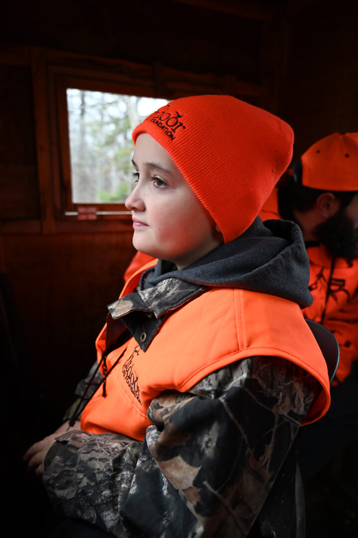 A young boy in an orange vest and hat.