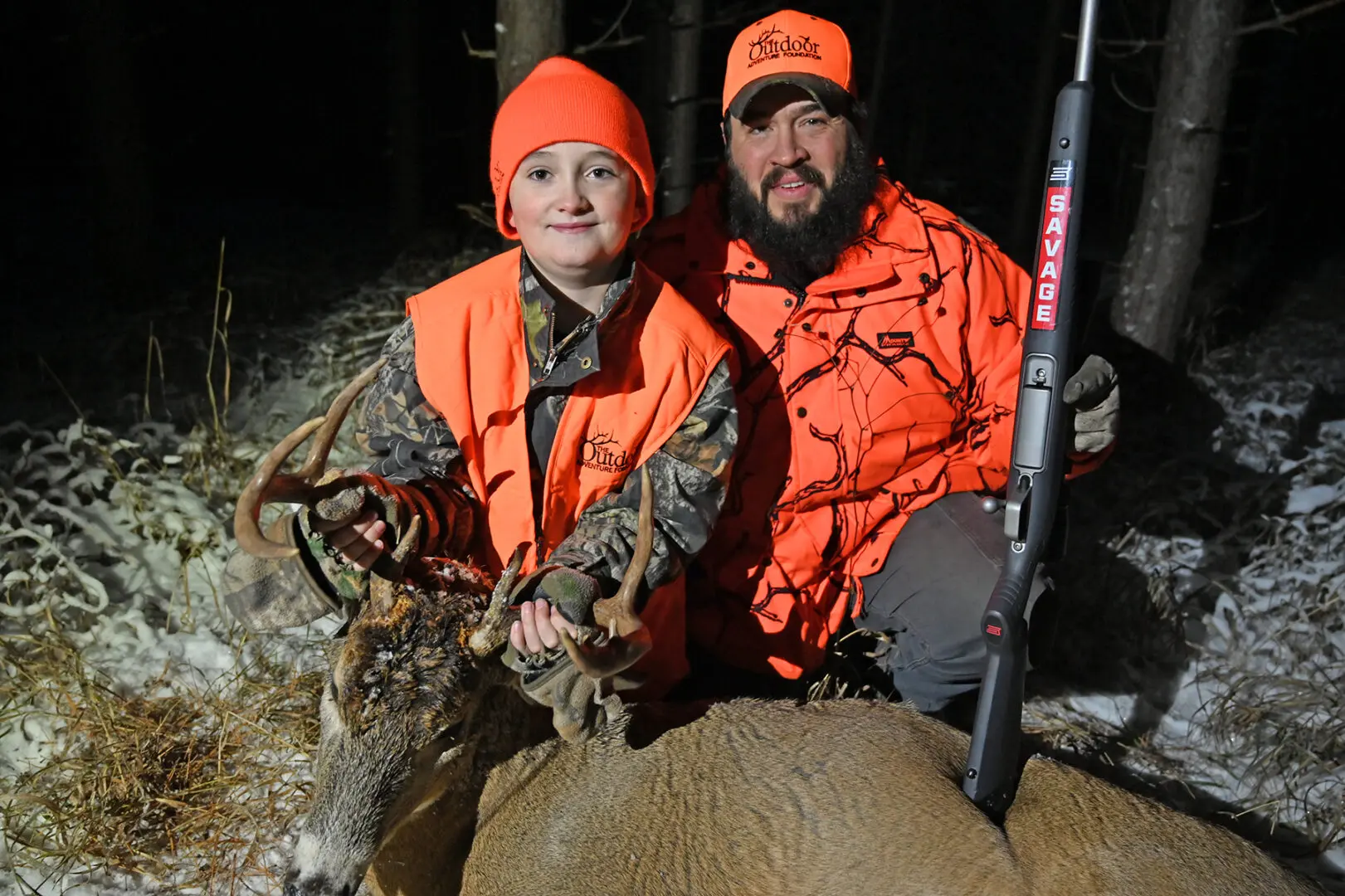 A man and woman in orange vests with deer.