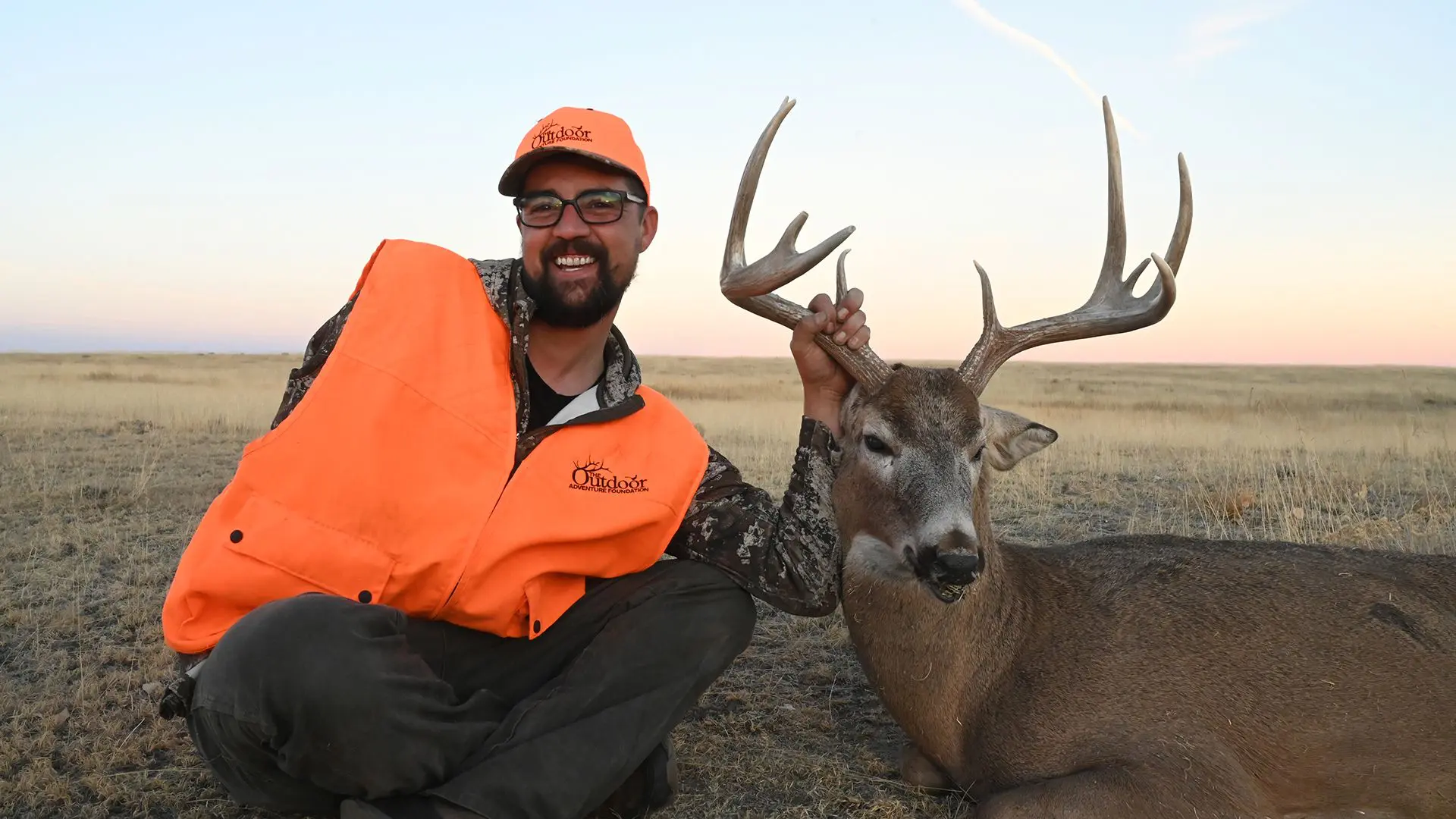 A man kneeling down next to a deer.