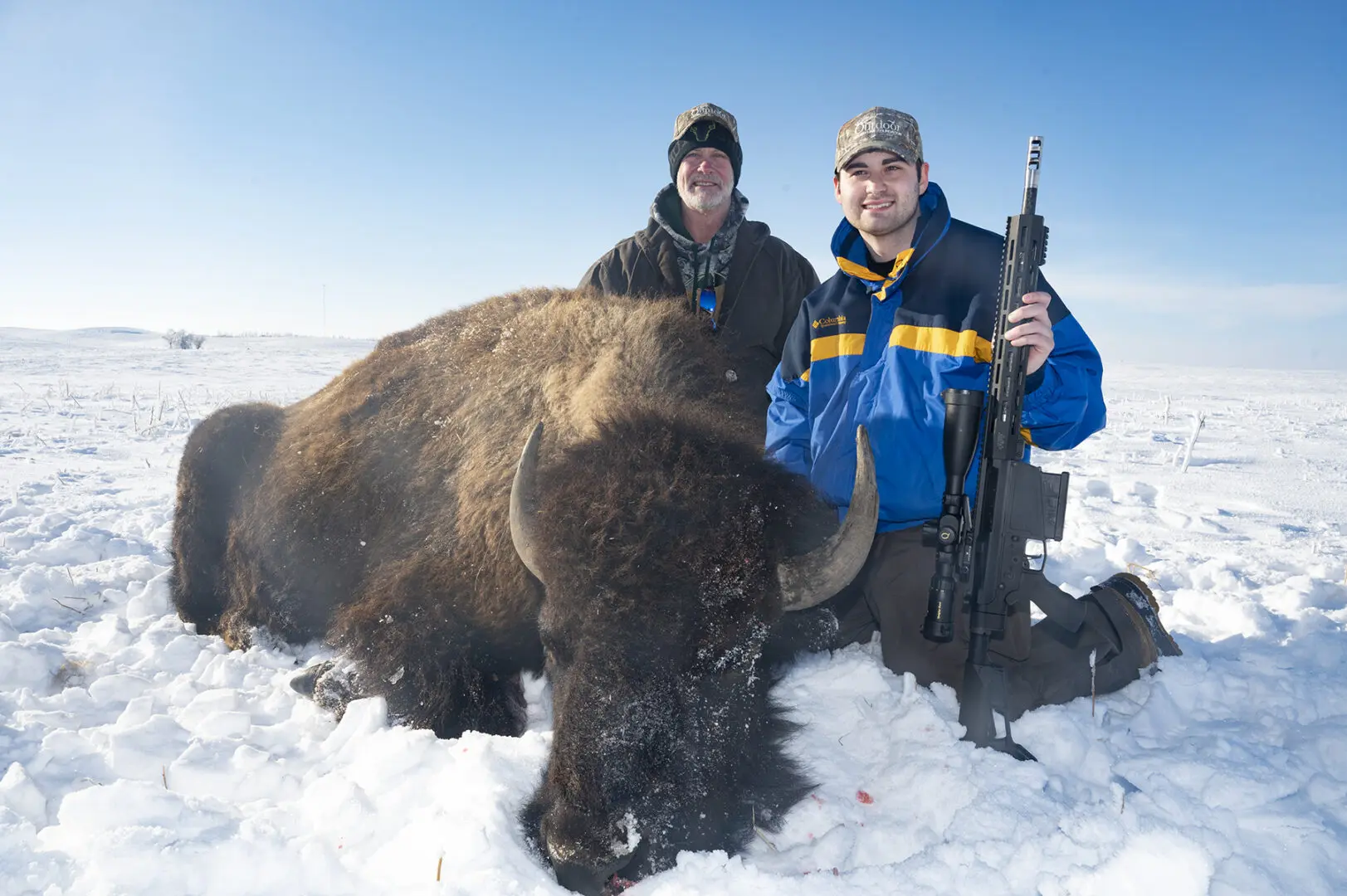 Two men standing next to a buffalo in the snow.