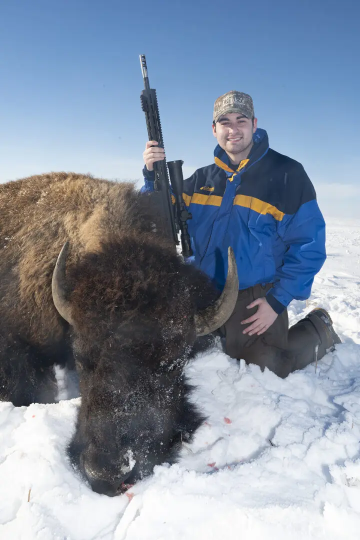 A man holding a rifle next to a bison.