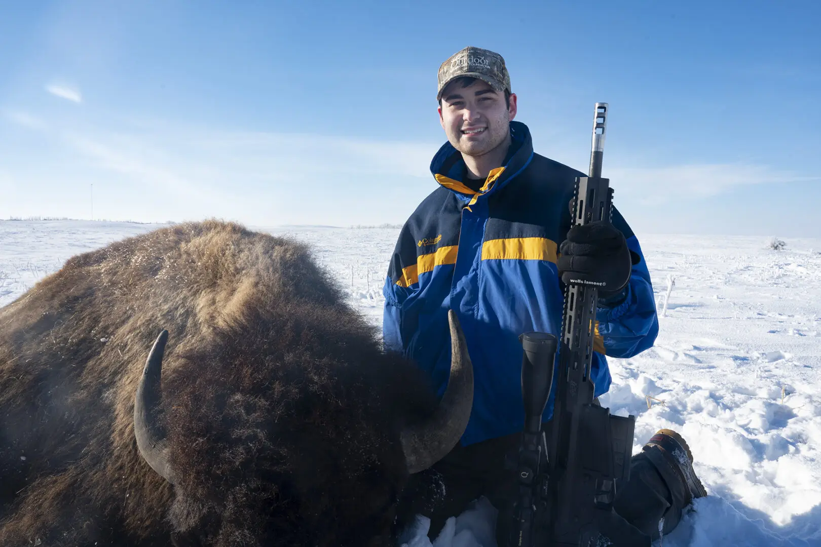 A man holding an automatic rifle standing next to a bison.