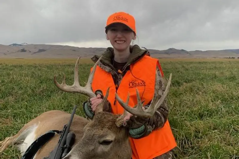 A woman in an orange vest standing next to a deer.