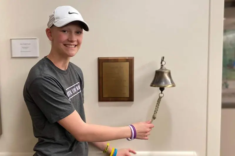 A boy in a white hat is holding a bell