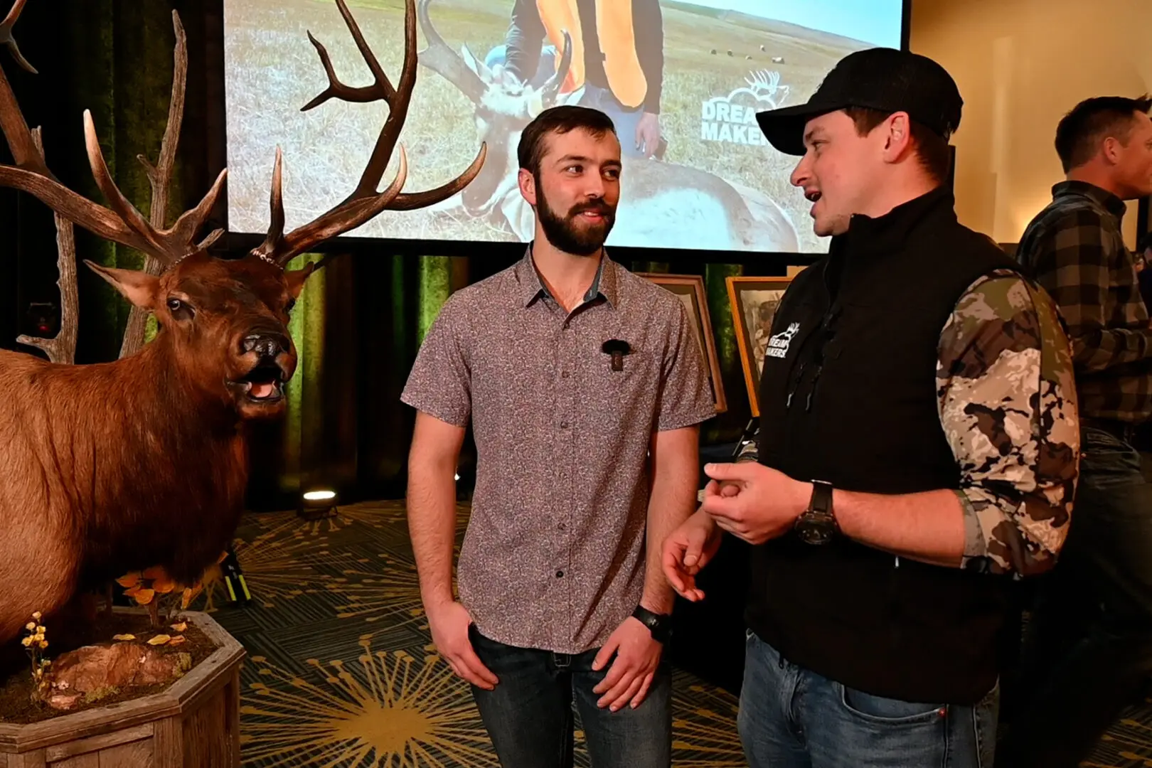 Two men standing in front of a screen with a deer.