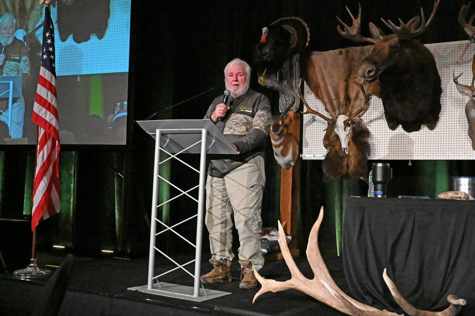 A man standing at a podium with an animal head on the wall behind him.