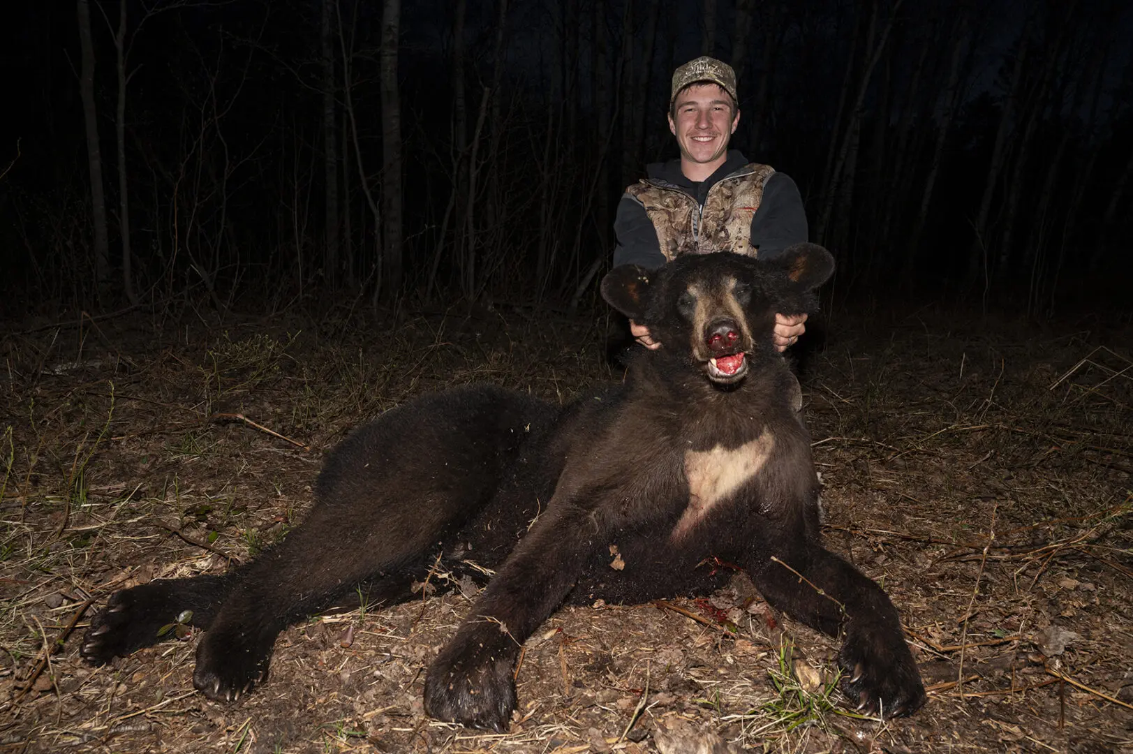 A man sitting on the ground with a large black bear.