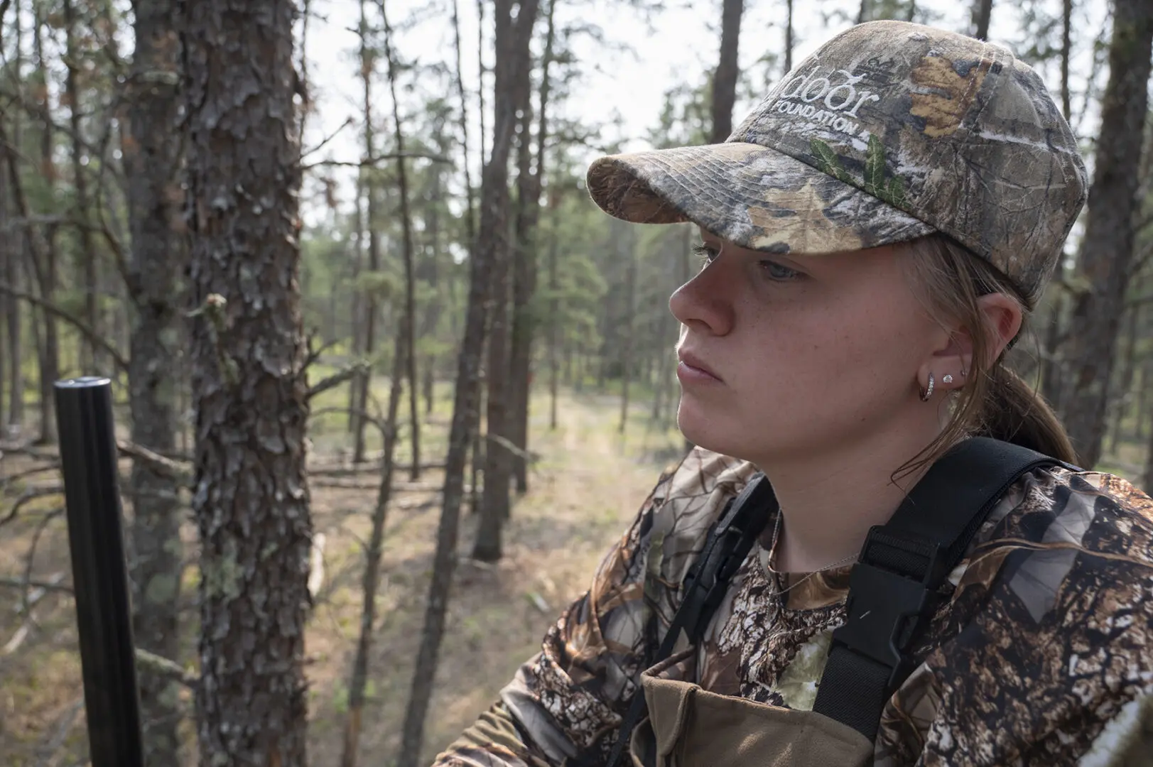 A woman in camouflage hat looking out at trees.