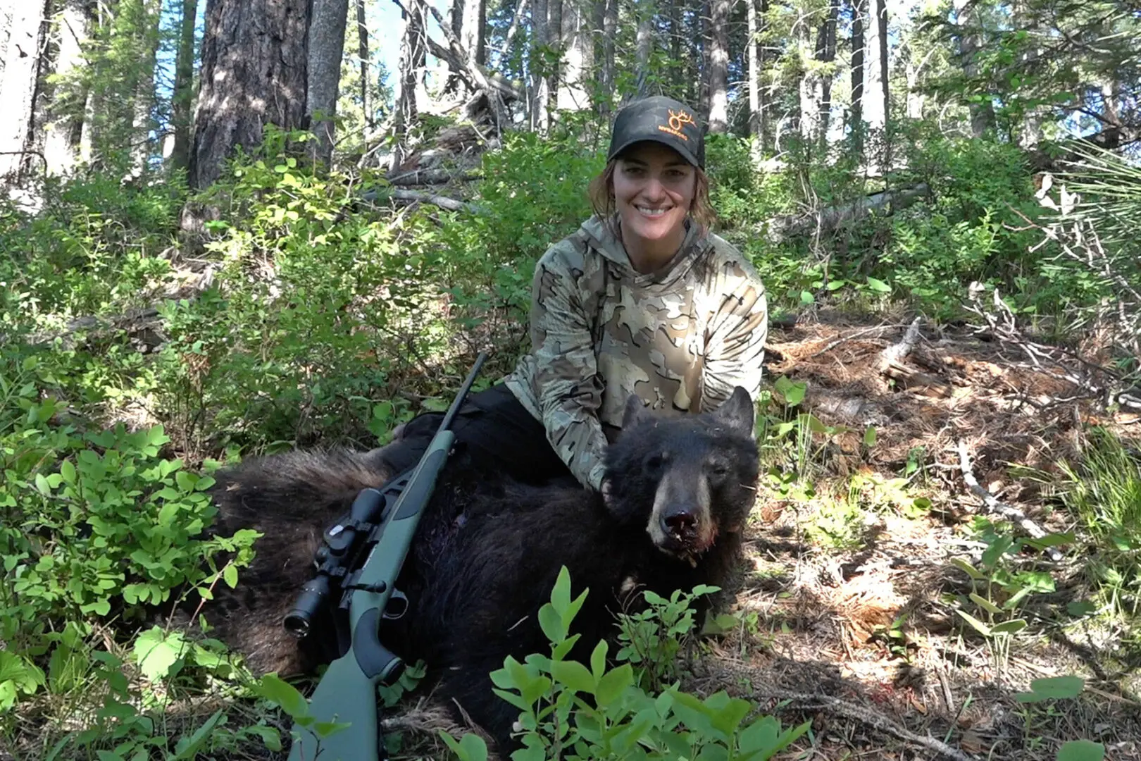 A woman in camouflage sitting on the back of a bear.