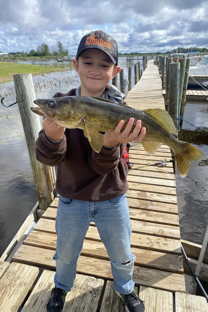 A boy holding a fish on top of a dock.