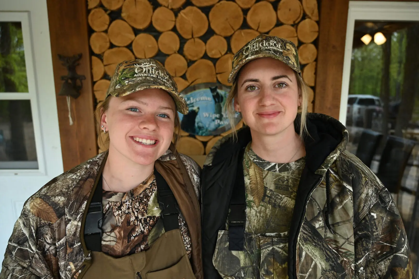 Two women in camo and hats are smiling.