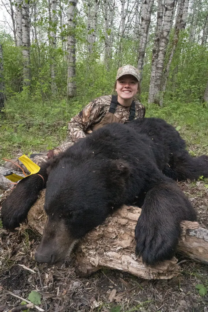 A woman in camouflage holding a bear while sitting on the ground.