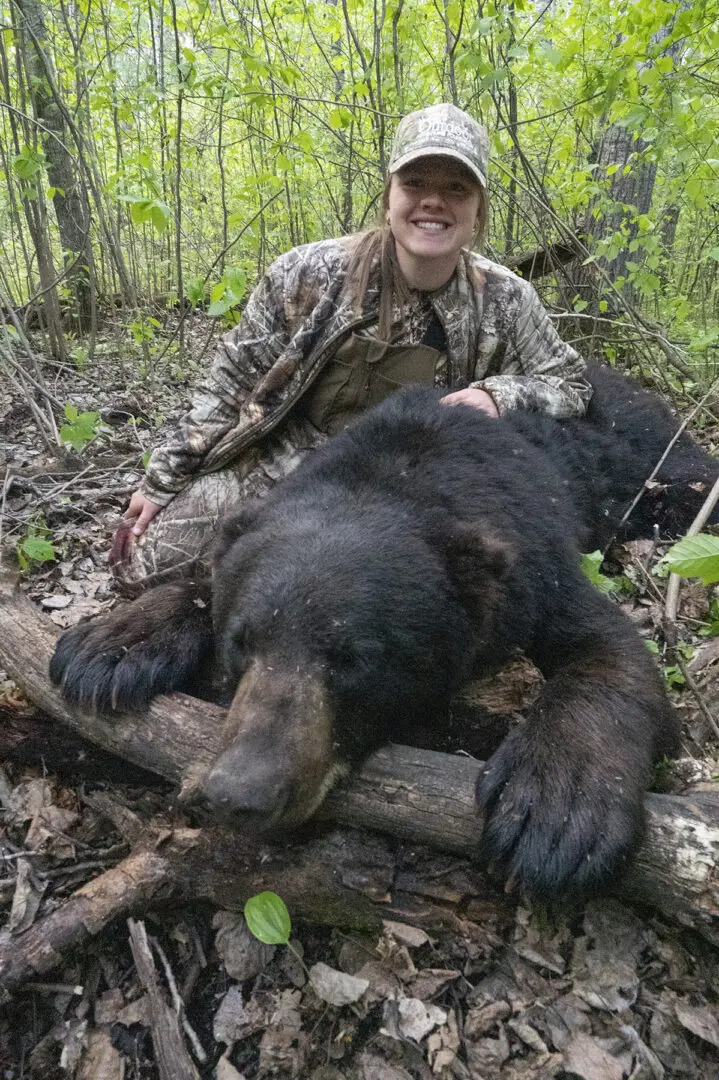 A woman in camouflage sitting next to a bear.