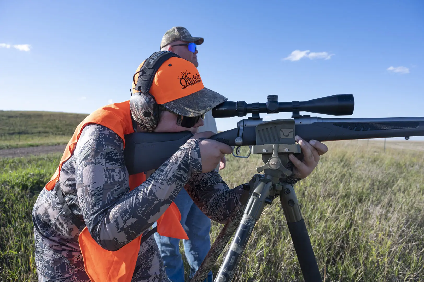 A man in an orange vest is holding a rifle