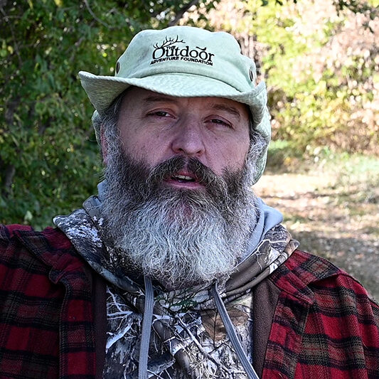 A man with long beard and hat in the woods.