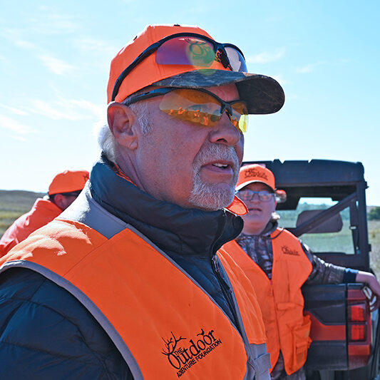 A man in an orange vest and hat standing next to another man.